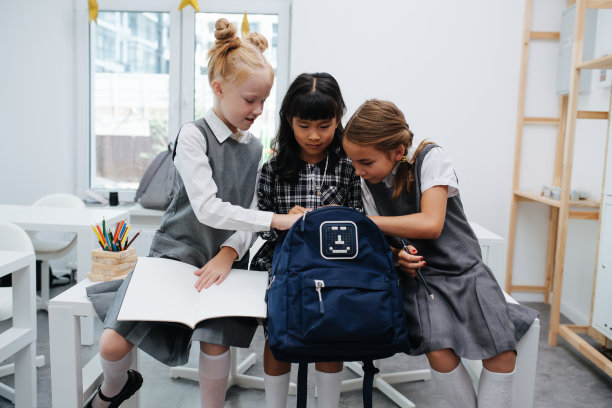 好奇的小女生们坐在课桌上，看着背包里的东西图片下载