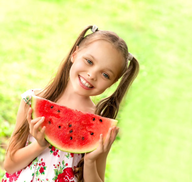 蓝眼睛的小女孩微笑着吃着一片西瓜图片下载