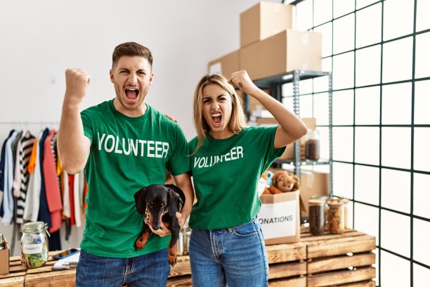 一对年轻夫妇带着可爱的狗，穿着志愿者t恤站在捐款站，愤怒而沮丧地大喊，愤怒而疯狂地大喊，并举起手来图片下载