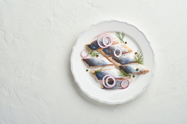 咸鲱鱼与香料，香草和洋葱在白色盘子上轻石背景复制空间。腌制切鱼。含有健康不饱和脂肪的食物，平铺图片下载