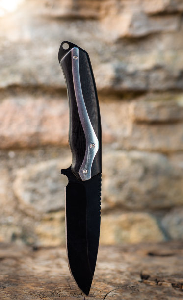 黑色露营或生存刀，木制和石头背景。户外生活方式图片下载