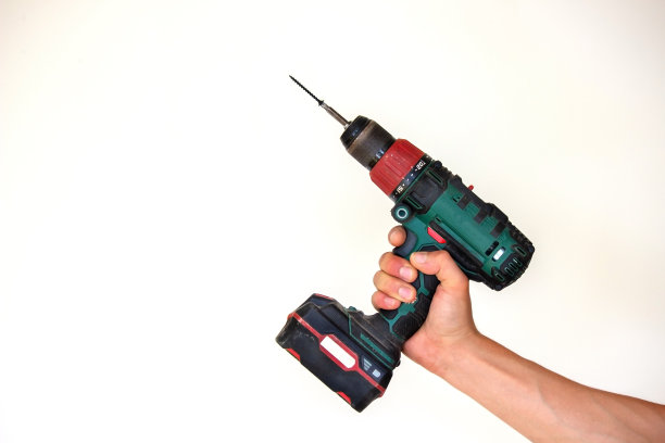 手持无绳螺丝刀和钻孔隔离在白色背景。将螺丝拧入板内。图片下载