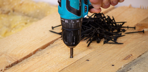 手持无绳螺丝刀和钻孔隔离在白色背景。将螺丝拧入板内。图片下载