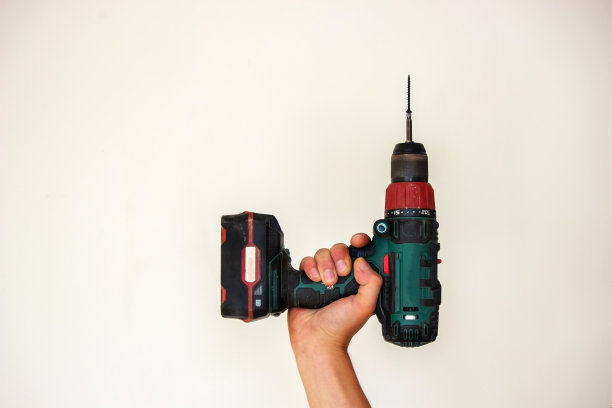 手持无绳螺丝刀和钻孔隔离在白色背景。将螺丝拧入板内。图片下载