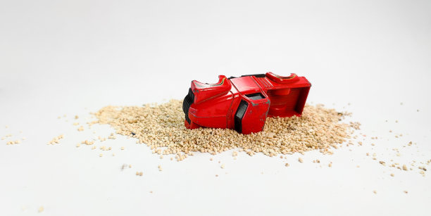 红色的旧玩具卡车在白色背景的沙滩上翻滚。图片下载