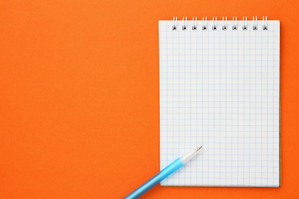 在橙色的背景上检查了笔记本和笔。与copyspace模型。图片下载