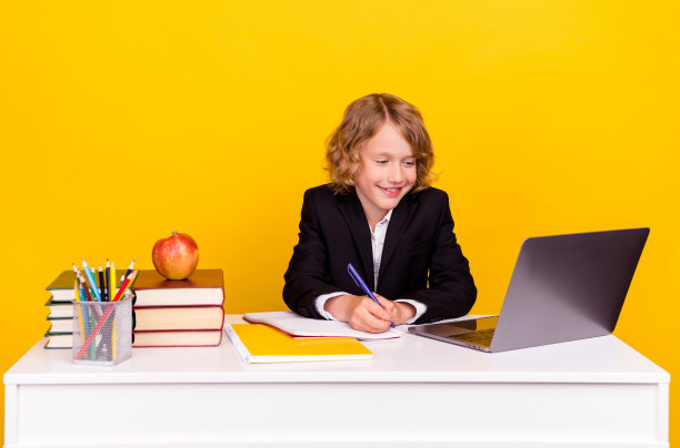 正聪明的学生坐着看上网本写笔记，穿着统一孤立的黄色背景照片图片下载