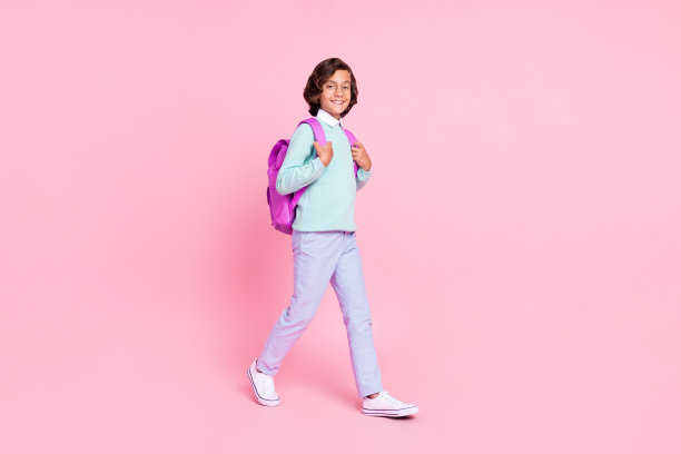 负责任的学生男孩走大学的照片，戴帆布眼镜，蓝绿色衬衫孤立的粉红色背景图片下载