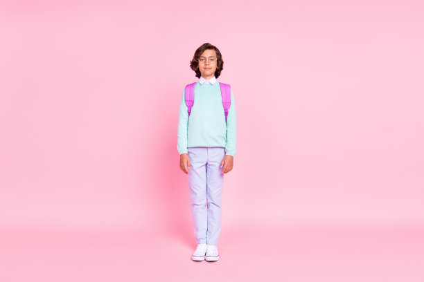 小男孩的照片看相机微笑戴背包眼镜蓝绿色衬衫孤立的粉红色背景图片下载