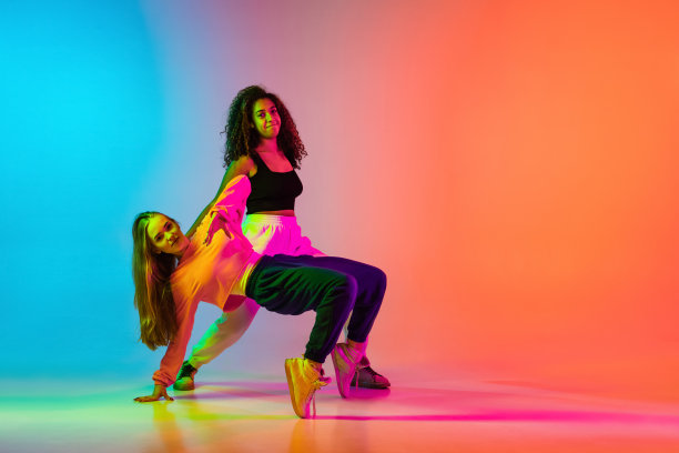 两个时髦的现代女孩在霓虹灯的渐变蓝橙色背景上跳嘻哈舞图片下载