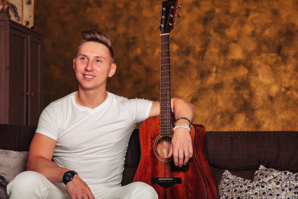 很棒的年轻人，穿着白色衣服，在室内拿着吉他图片下载