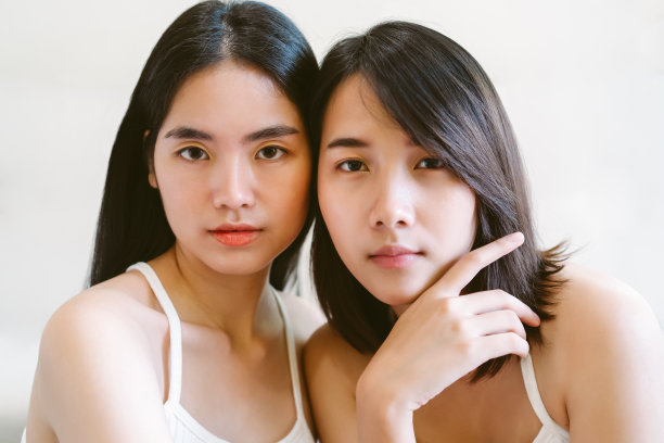 两个美丽的年轻亚洲妇女的肖像看着相机孤立在白色的墙壁背景。护肤、美容与健康女性。图片下载