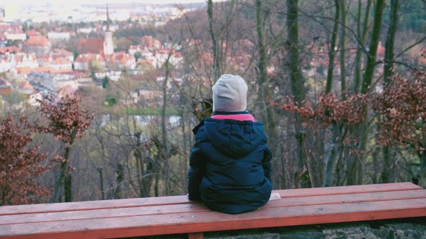 孩子穿着暖和的衣服坐在观光点的长凳上从远处的山顶看欧洲城市全景图片下载