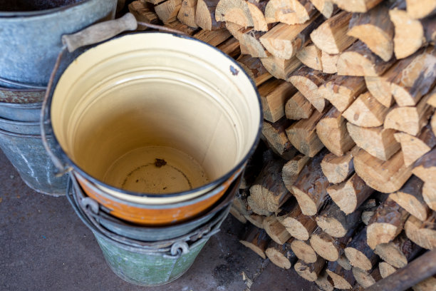 破旧的金属桶立在棚子里，旁边是一堆劈好的柴火图片下载