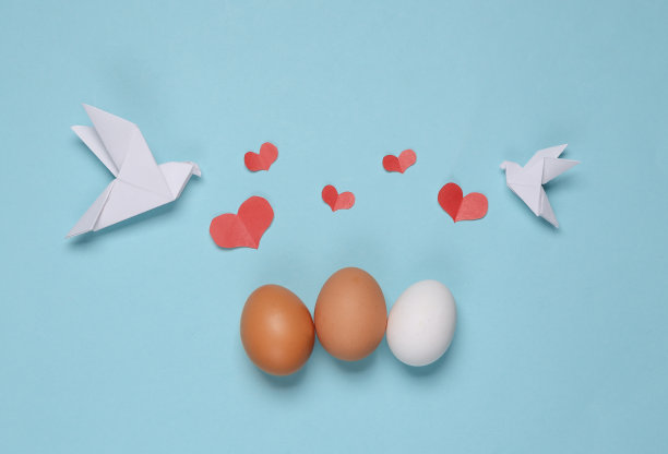 蓝色背景上有心形和鸡蛋的折纸鸽子。春天,复活节的概念图片下载