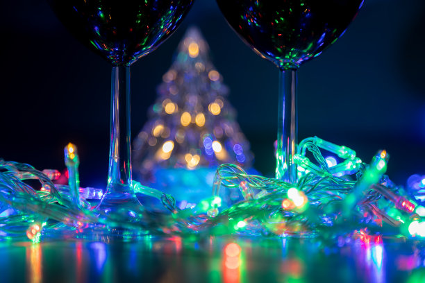 两盏玻璃杯放在一棵闪亮的圣诞树的背景上，一个五彩缤纷的花环放在黑夜的背景上。新年庆祝活动……图片下载