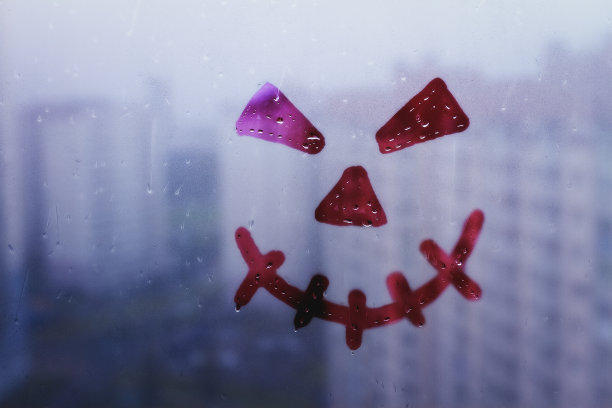 窗户上画着可怕的红脸和邪恶的眼睛，模糊的蓝色玻璃背景上满是雨滴图片下载