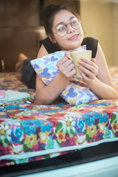 漂亮的年轻女子躺在床上，拿着咖啡杯，在沉思。图片下载