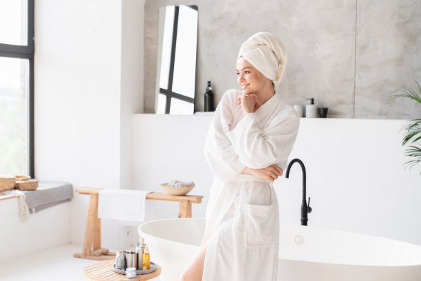 快乐的年轻女子在温泉浴袍和毛巾使用化妆品淋浴后在家里。美容治疗，身体及皮肤护理。图片下载