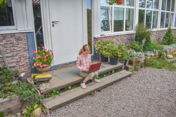 一个女孩带着笔记本电脑坐在房子的门廊上上课，在没有滤镜的远程照片上图片下载