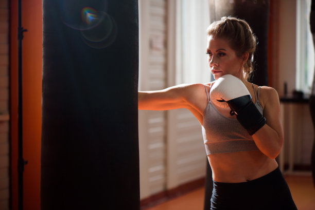 一名年轻女子在体育馆里练习拳击，她戴着拳击手套，在拳击袋上挥拳。图片下载