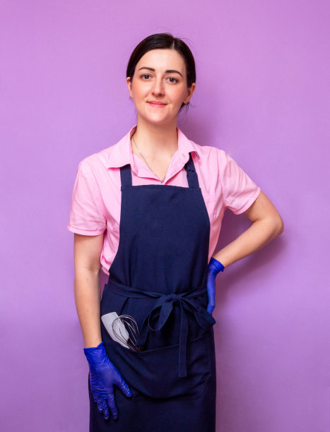 一个穿着围裙和手套的糕点女厨师的肖像。围裙的口袋里有一把厨房用的打蛋器和一把刮刀。有选择性的重点。图片下载