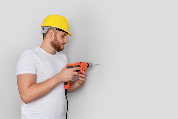 一名工人正在墙上打孔以便建筑或翻新。图片下载