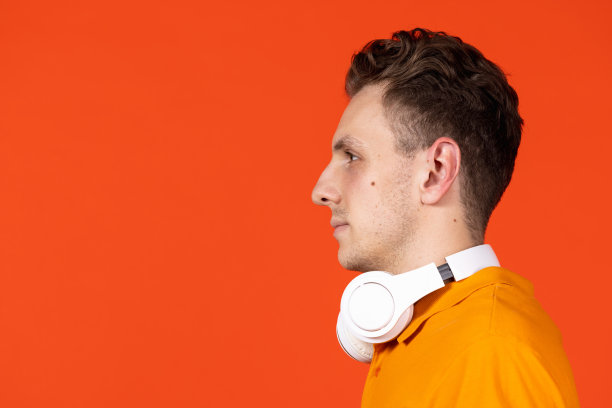特写照片的年轻白人男子在耳机孤立在橘色工作室背景。概念人类的情感，面部表情，青春，感情，广告。图片下载