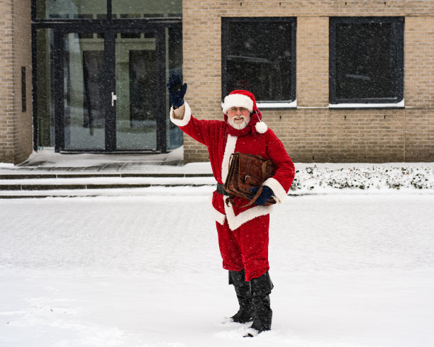 圣诞老人商人的问候。圣诞节盛宴。商人圣诞老人穿着传统服装，手里拿着公文包，站在雪地里。图片下载