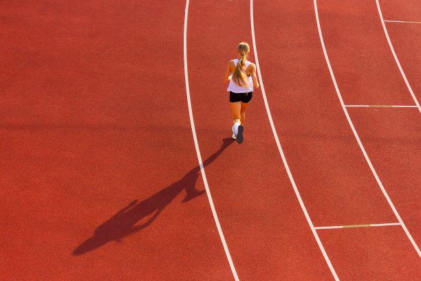 一个穿着运动服的年轻女子沿着体育场的跑道奔跑，向后看。图片下载