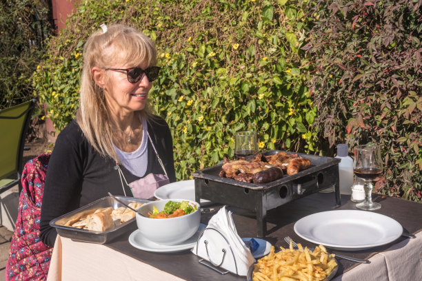 一名成年女子坐在餐桌旁，微笑着看着阿根廷烤肉、沙拉和炸薯条。图片下载