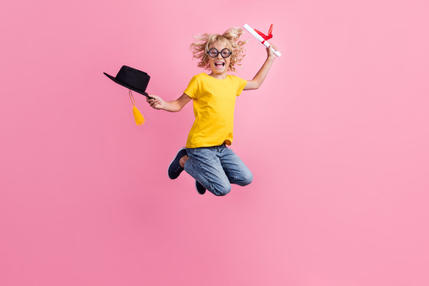 年轻的学校男孩的全身照片快乐积极的微笑跳毕业文凭孤立在粉红色的背景图片下载