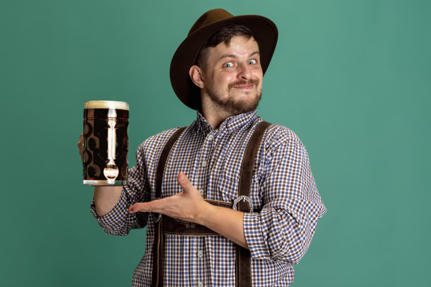 身着巴伐利亚传统服装、蓄着胡须的男子肖像，在绿色背景下孤立地喝着一升深色啤酒。十月啤酒节,节日的概念图片下载