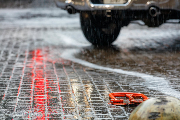 大雨冲刷着停车场一排排平坦的铺路板，反射着红绿灯的红光。图片下载
