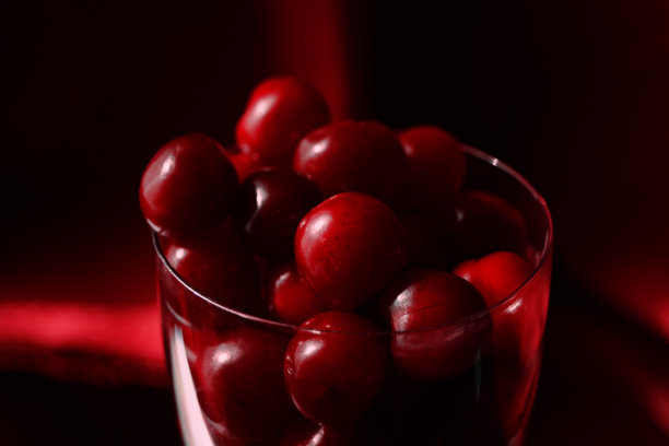 新鲜多汁的樱桃或快乐在一个玻璃特写暗红色背景在一个低调。图片下载
