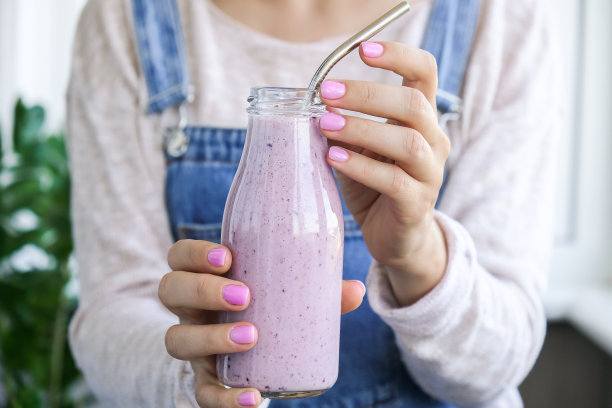 女手握蓝莓奶昔顶部的蓝莓。一名女子正在吃由生蓝莓泥、香蕉、牛奶、酸奶和白软干酪制成的蛋白质早餐饮料图片下载