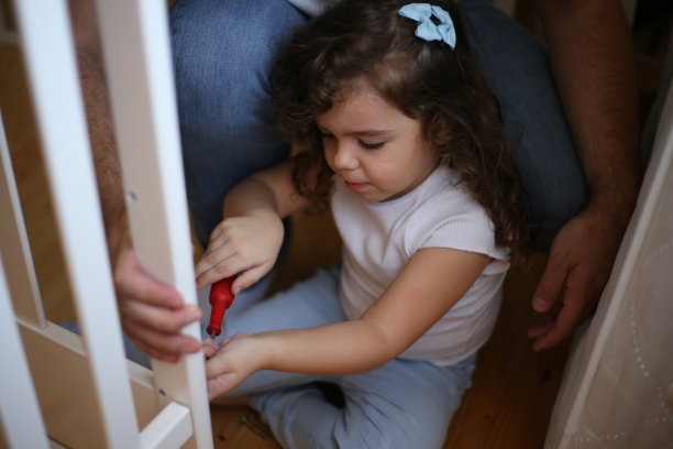 小女孩帮她爸爸组装婴儿床。库存图片图片下载