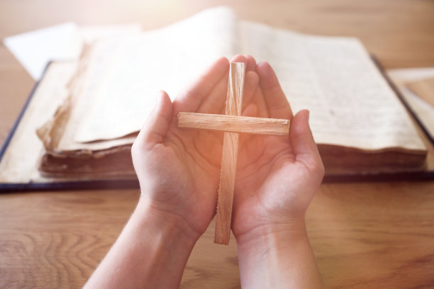 手持木十字架的妇女在旧圣经上祈求上帝的祝福，阳光的背景，希望的概念图片下载