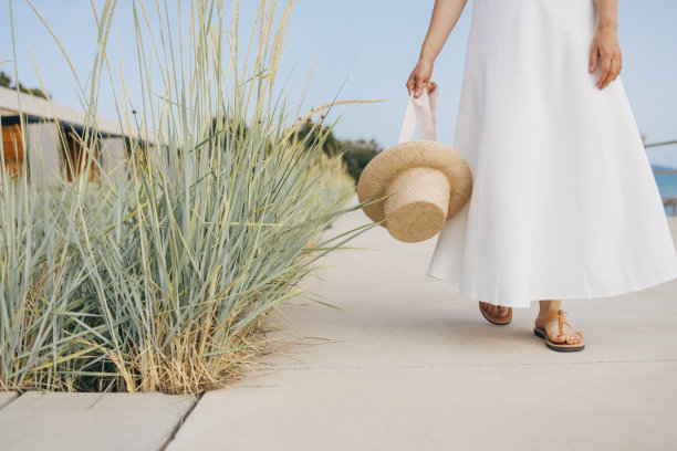 身穿白色连衣裙的无名女子，戴着帽子，走在高高的草丛旁图片下载