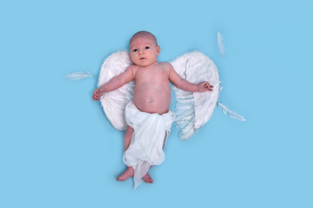 一个有着白色天使翅膀的新生男婴在一个蓝色背景的工作室里，复印空间。一个穿着尿布的白人婴儿一个月大图片下载
