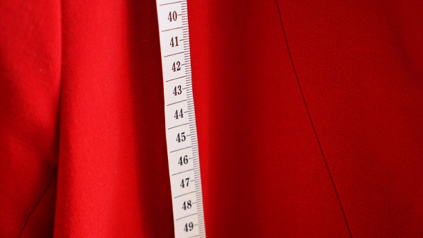 白色的卷尺放在外套红色布料的背景上。图片下载