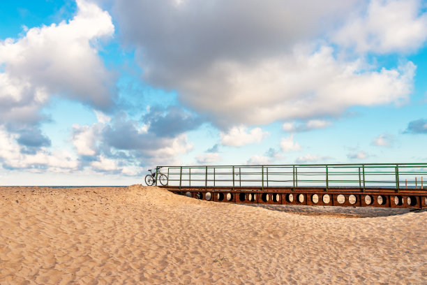 沿着波罗的海沿岸的一条自行车道，在干涸的河口上有一座自行车桥通向大海。那辆自行车靠在桥的栏杆上。美丽的蓝天和一片沙滩图片下载