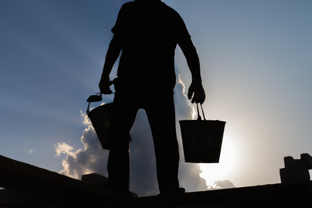 在天空的背景下，一名建筑工人的剪影，手里拿着水桶图片下载