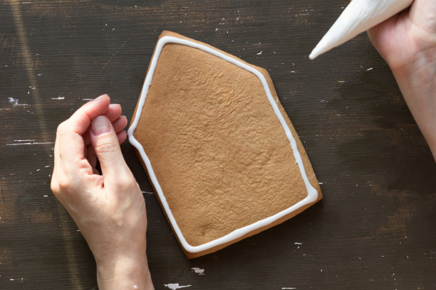 俯视图的妇女手装饰姜饼屋的糖霜图片下载