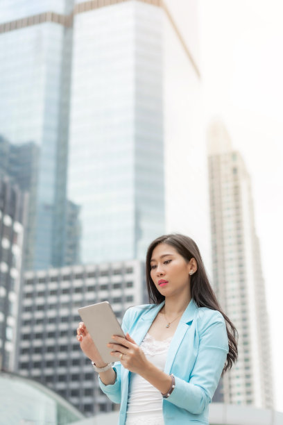美丽可爱的女孩穿着商务女装，手持智能手机平板电脑上的商务区城市背景，商业理念图片下载