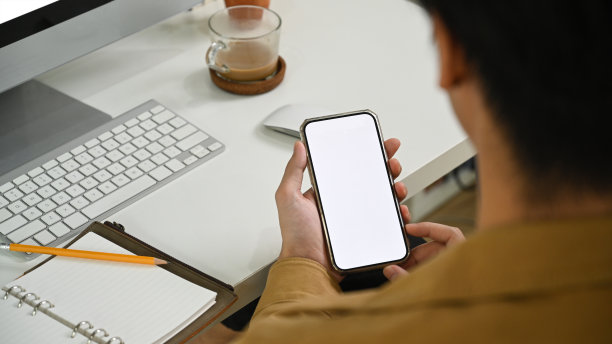 年轻人坐在工作场所使用智能手机的后视图。图片下载