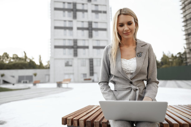 年轻漂亮的女商人坐在街上的长椅上用笔记本电脑工作图片下载