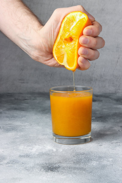 一个人正在盛满新鲜橙汁的杯子里挤桔子汁图片下载