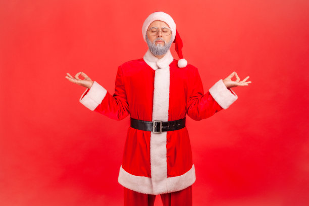 灰胡子老人穿着圣诞老人的服装，闭着眼睛冥想，心平气和地放松，练习瑜伽。图片下载