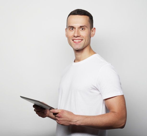 科技和生活理念:年轻男子穿着白色t恤使用平板电脑孤立在灰色背景图片下载